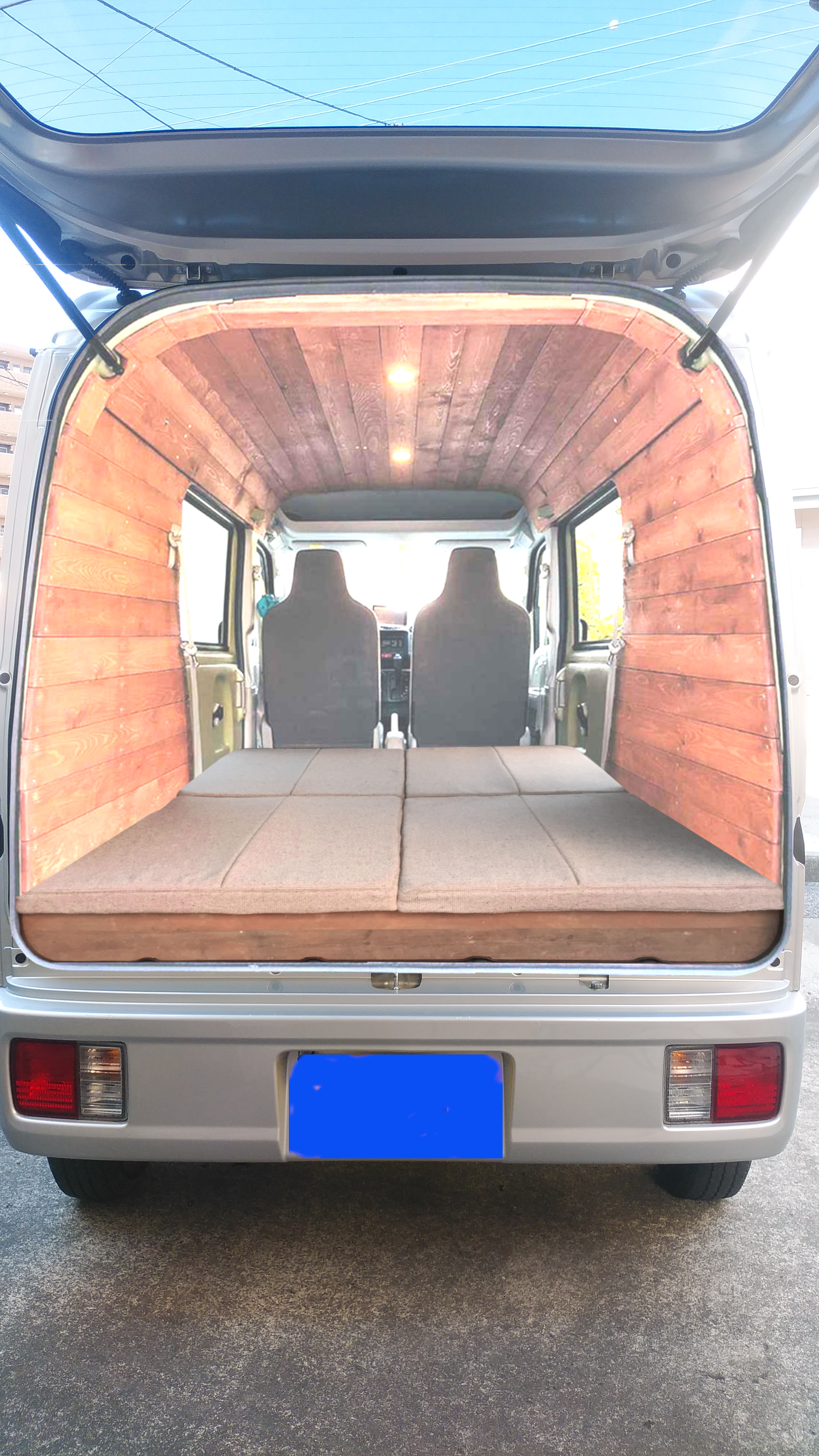 バックドアを開けた軽バンの荷室。壁と天井を板張りにし、ベッドマットを敷いたバンライフ仕様