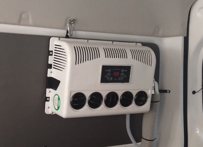 荷室壁面に取り付けた白い12Vエアコン室内機。丸形吹き出し口5連とデジタル操作パネル、断熱材を巻いた配管